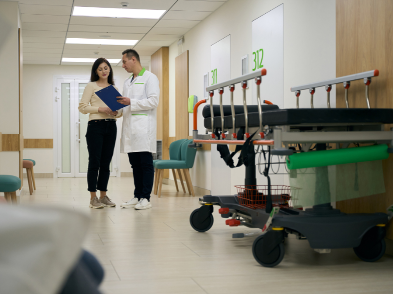 Funcionário conversando com paciente em corredor hospitalar.